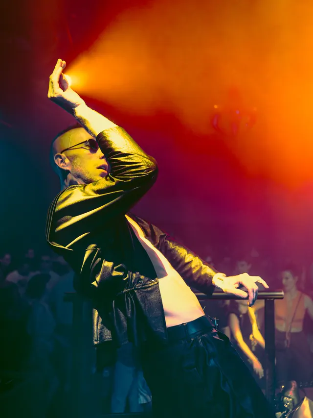 Performer raising a hand beneath deep red and amber stage light.