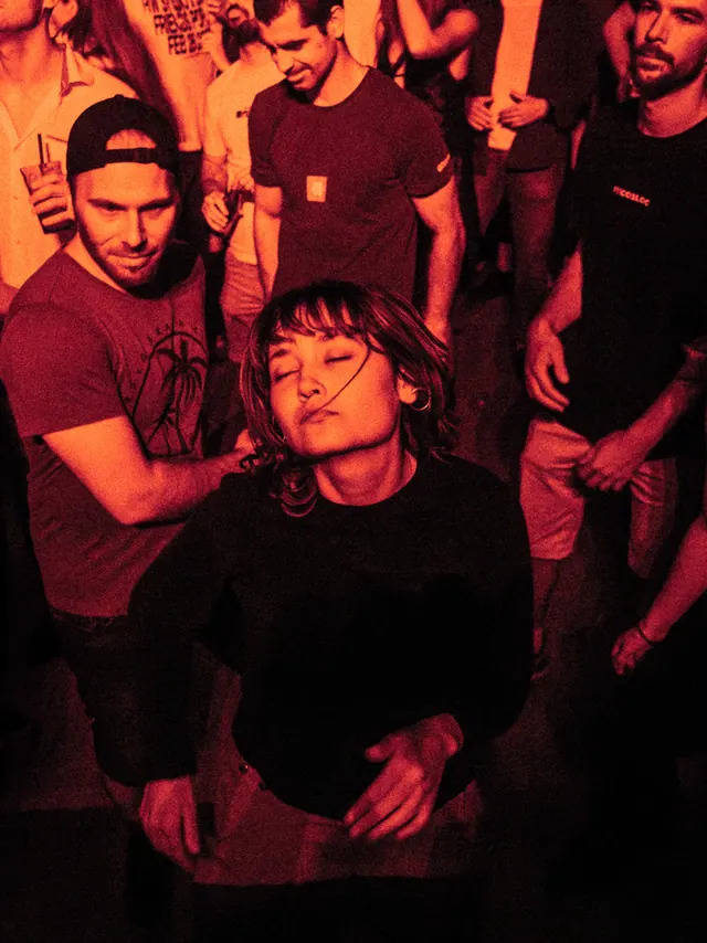 People dancing together in the warm red light of a club night.