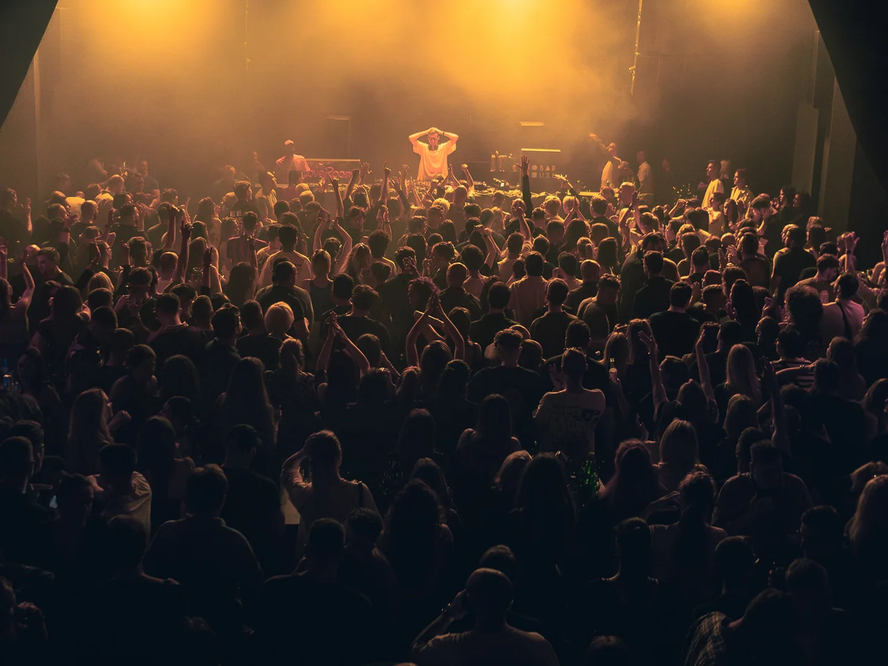 Large concert crowd gathered beneath golden haze and stage lights.