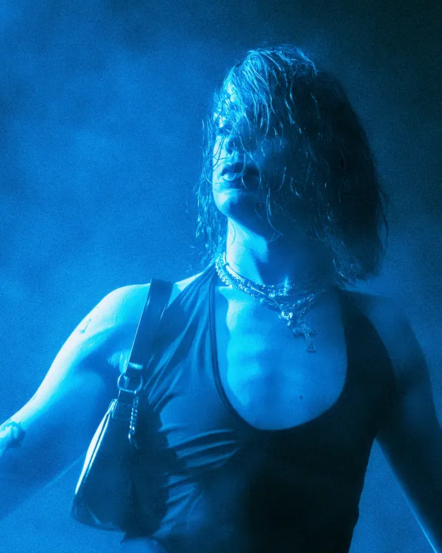 Close portrait of a dancer lit in turquoise during a club night.