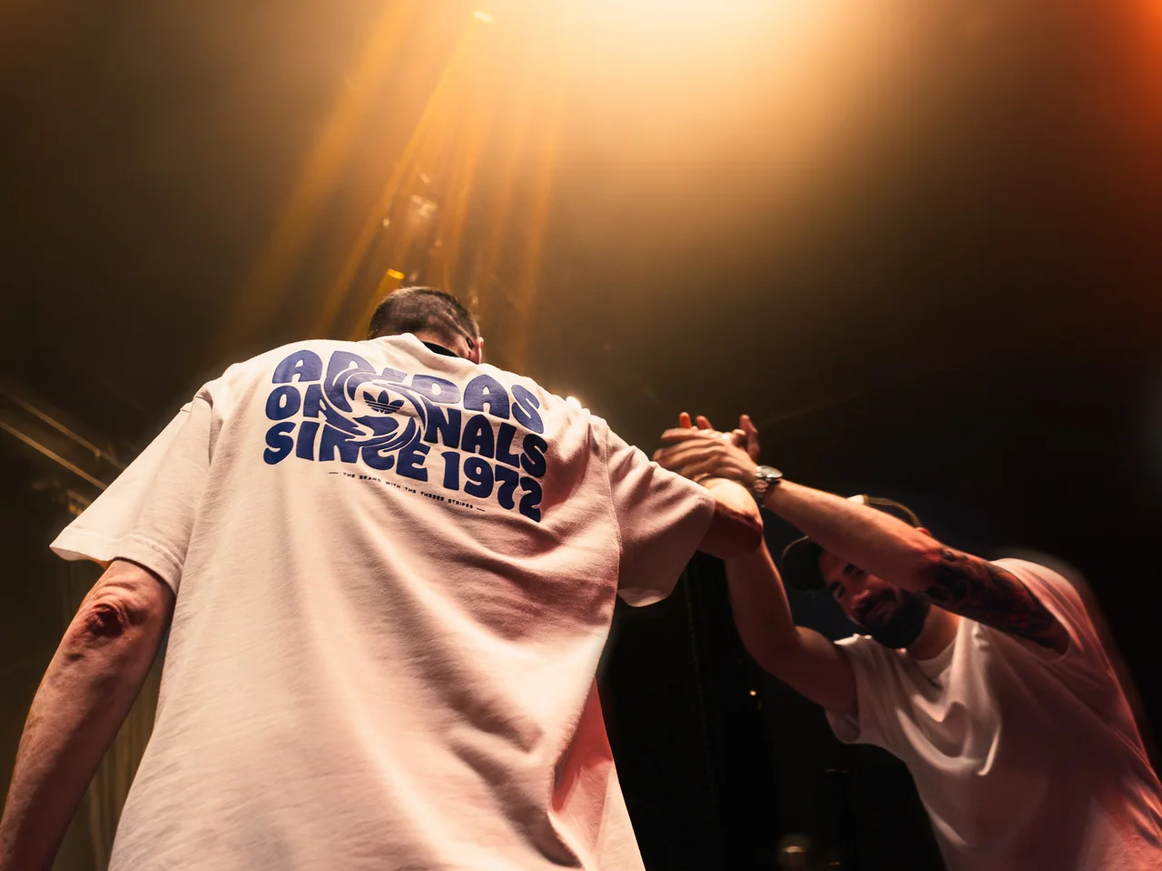 Two people greeting each other beside the stage at a live event.