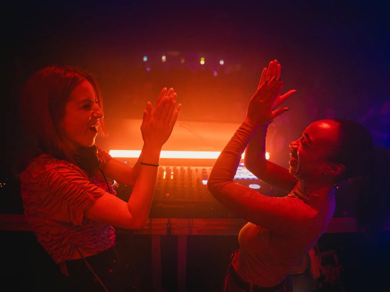 Two women dancing face to face beneath red club lighting.