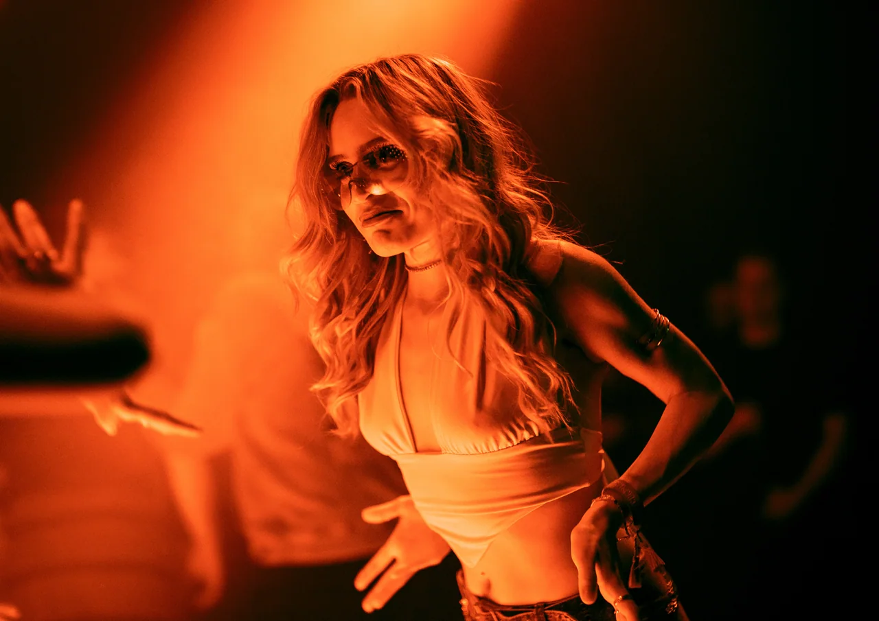 Woman dancing in a vivid pool of orange stage light.