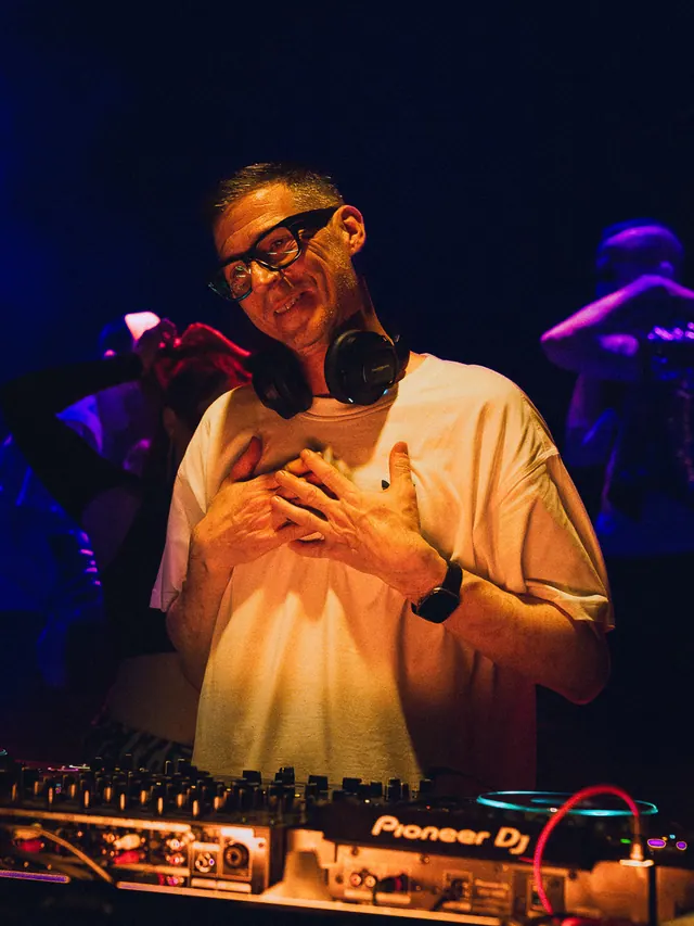 DJ holding a hand to their chest during a purple-lit set.