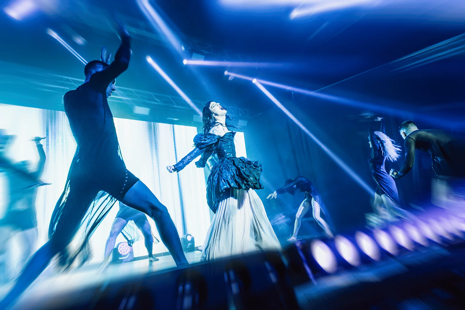 Performers crossing a blue-lit stage during a choreographed show.