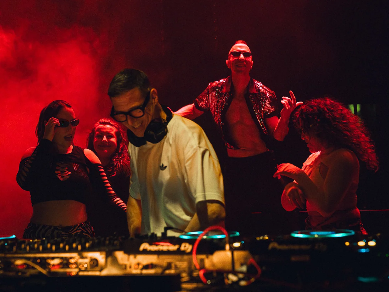 DJ and dancers framed by intense red light at the booth.