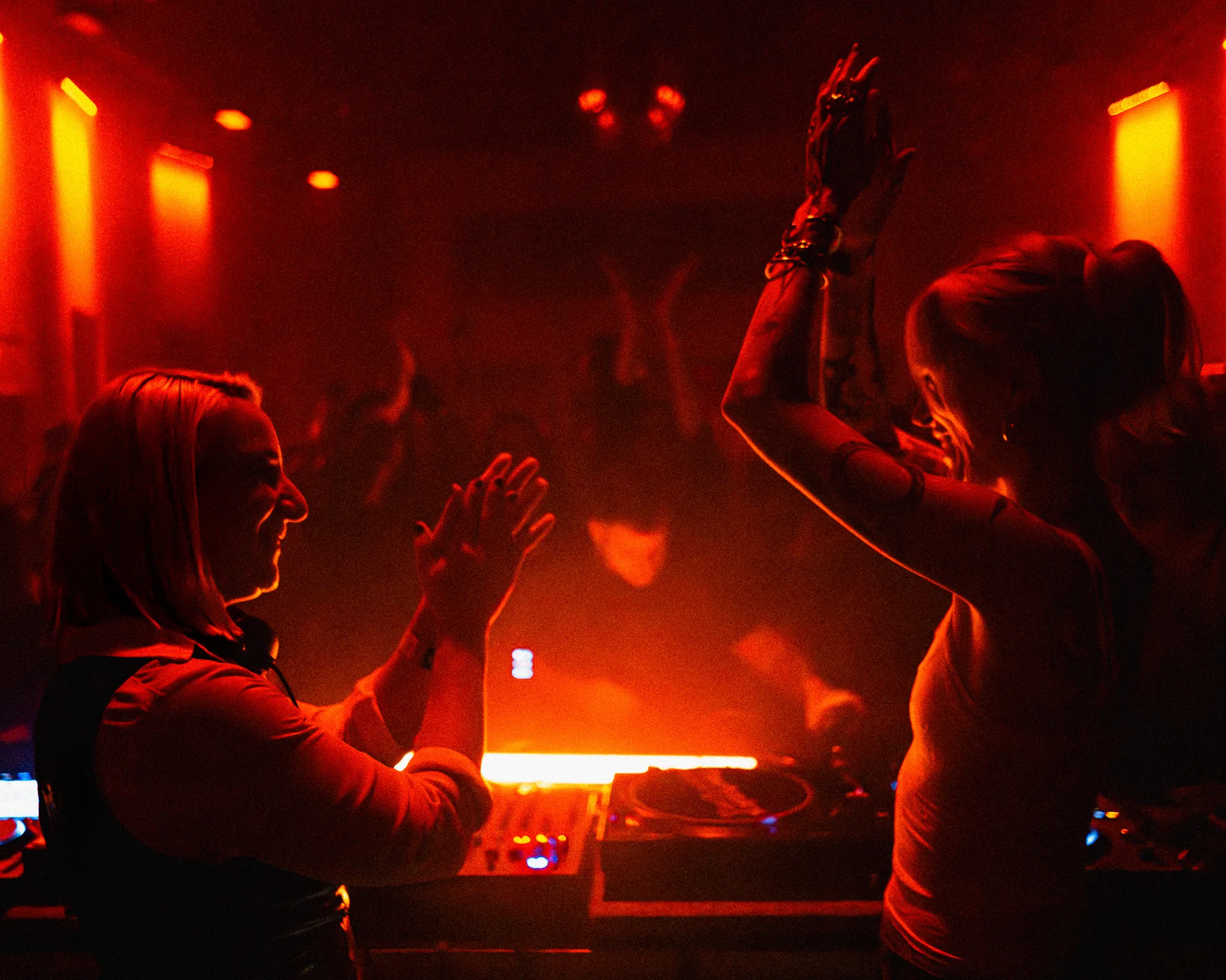Silhouetted crowd dancing beneath red lights and haze.