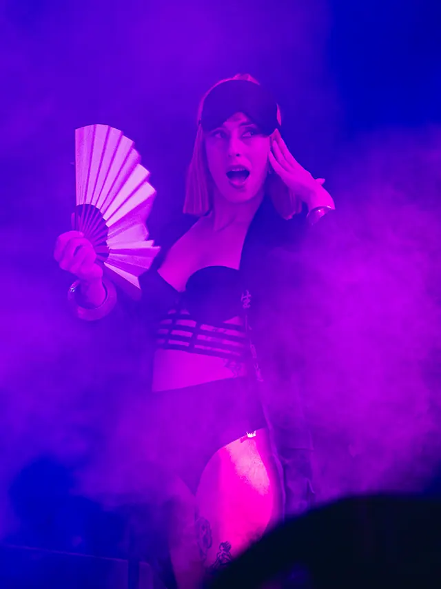 Woman reacting with a folding fan in vivid purple light.