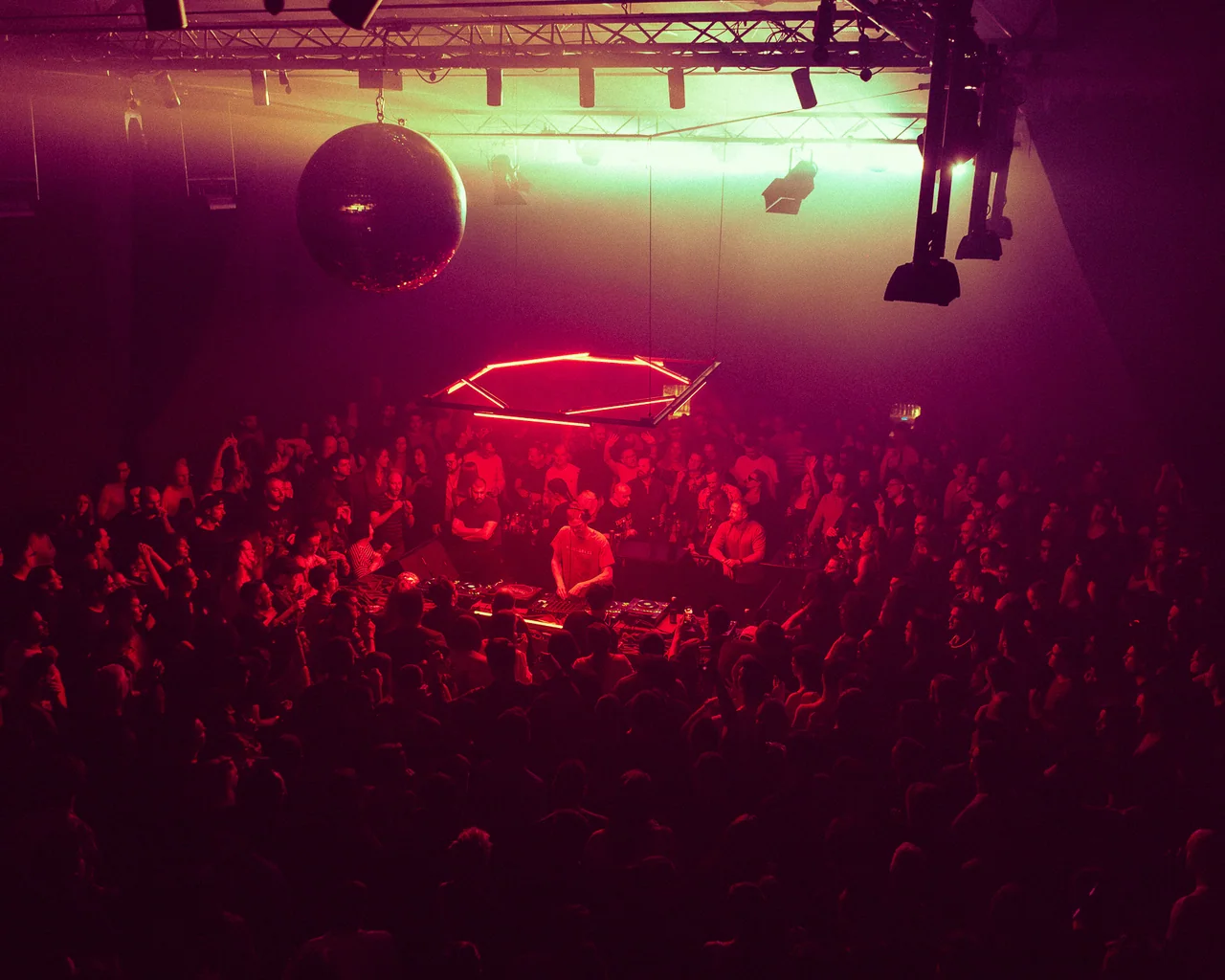 Packed dance floor seen from above beneath magenta lighting.