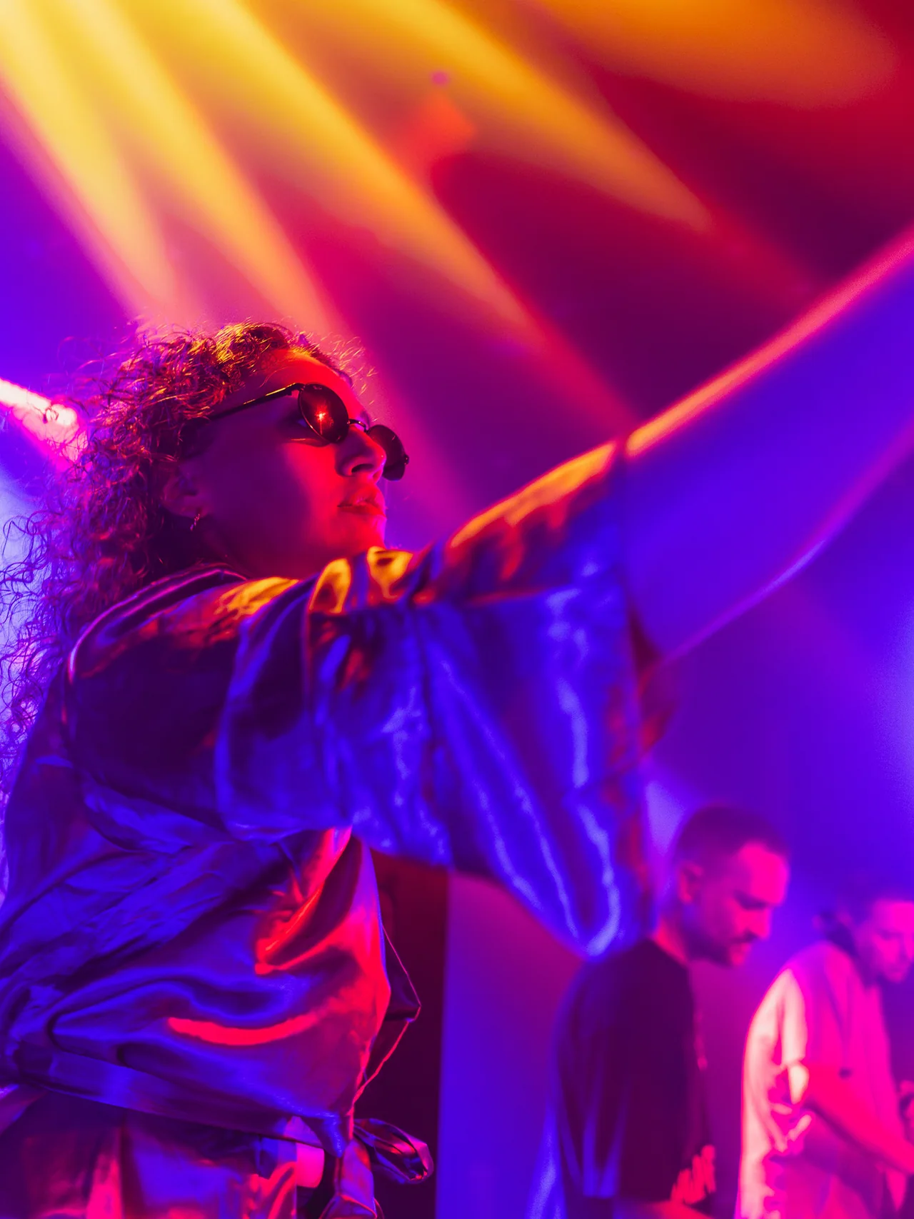 Performer beneath sharp orange beams and saturated purple light.