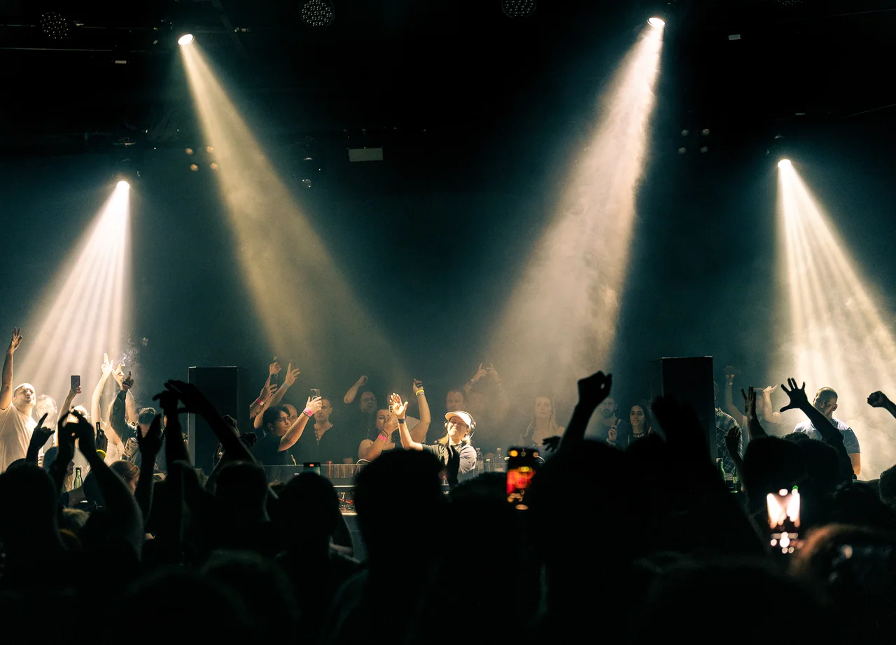 Audience silhouettes framed by two white spotlights and stage haze.