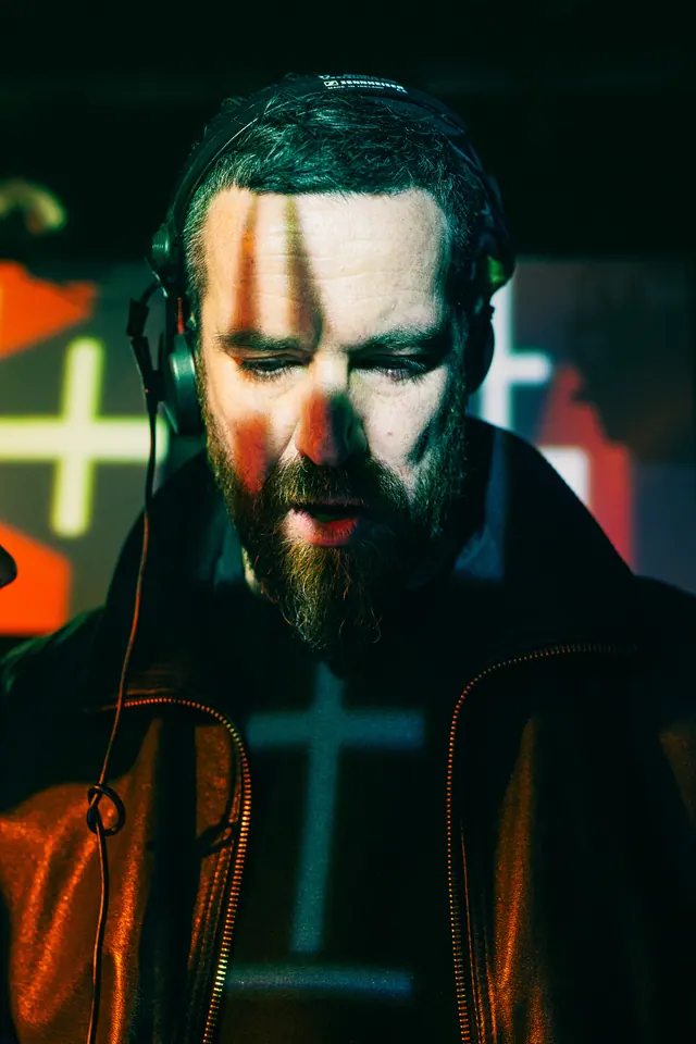 Close portrait of a DJ patterned by green and amber projection light.