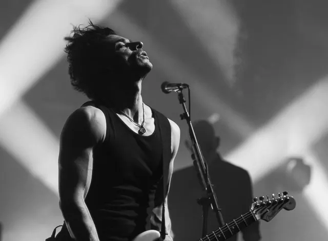 Singer in profile at the microphone during a black-and-white live set.