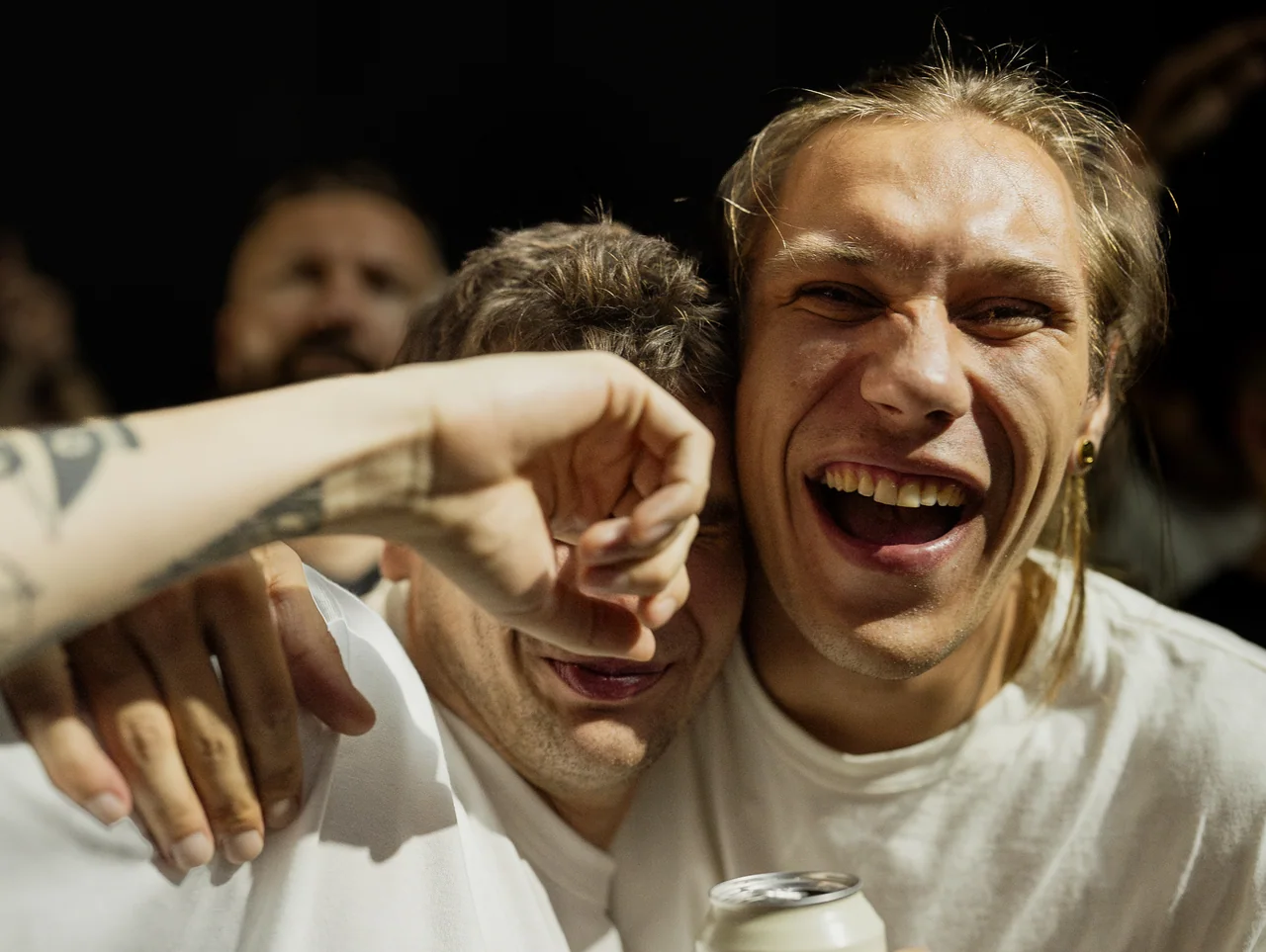 Two friends laughing and leaning into the camera at an event.