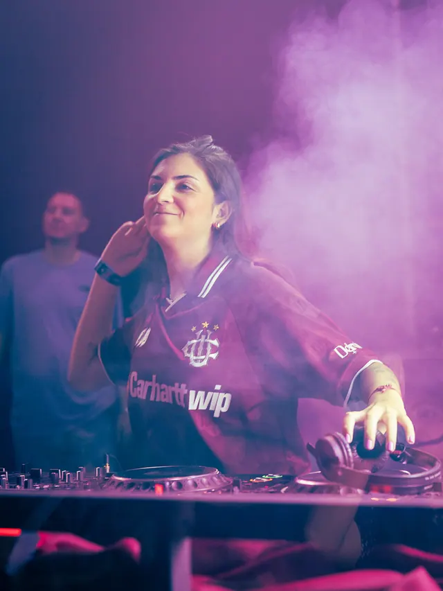 Woman wearing headphones at a hazy purple-lit event.
