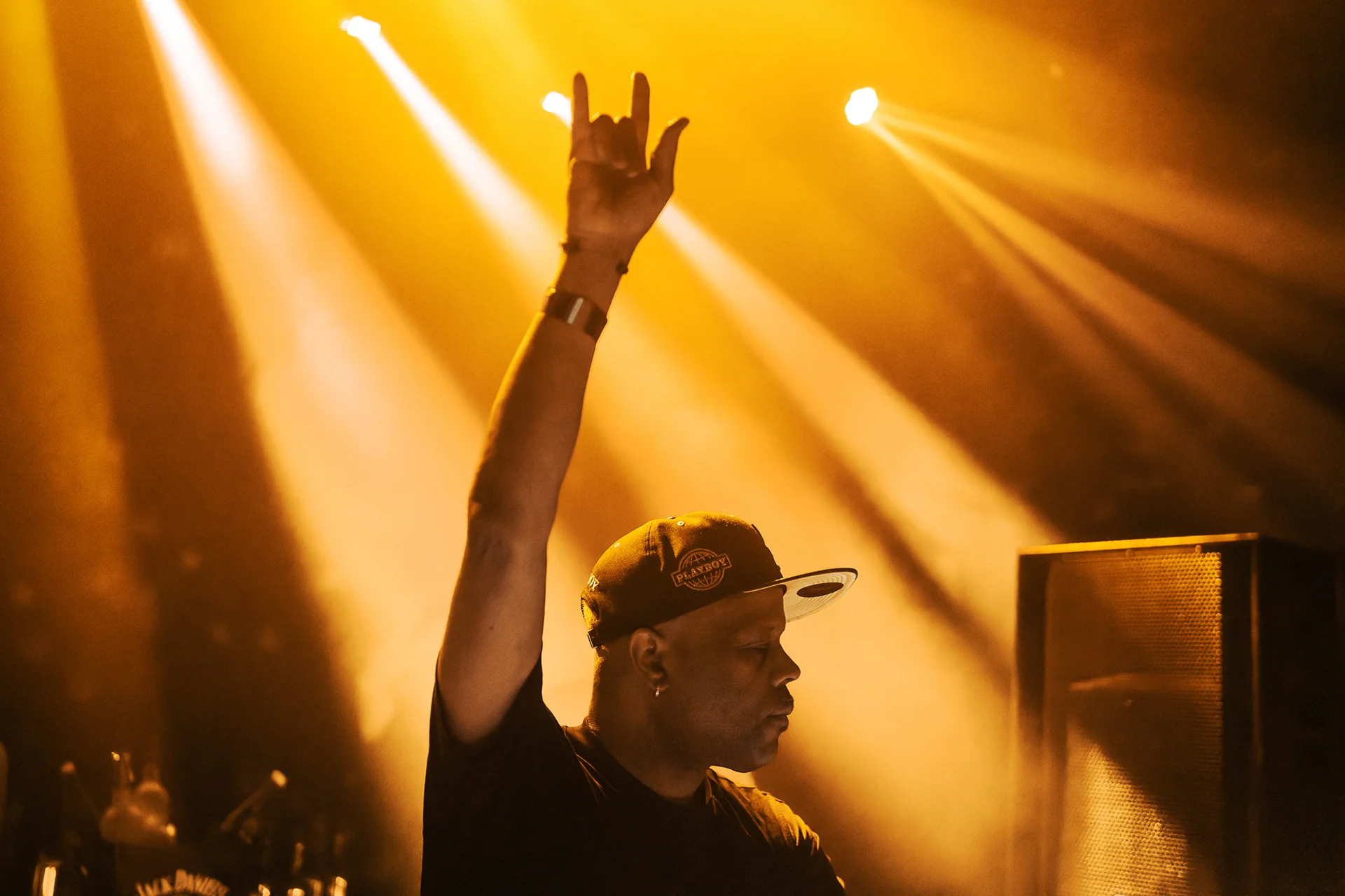 Performer holding a microphone beneath radiating amber spotlights.