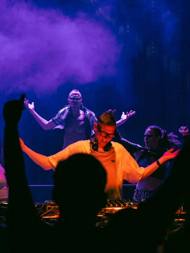 DJ performing with dancers on stage beneath blue and red light.