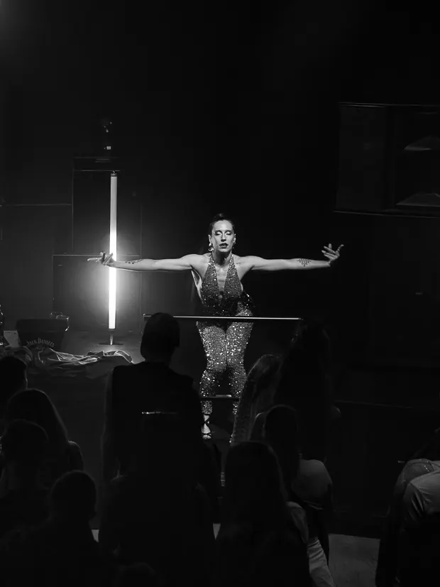 DJ with arms outstretched between vertical lights on a dark stage.