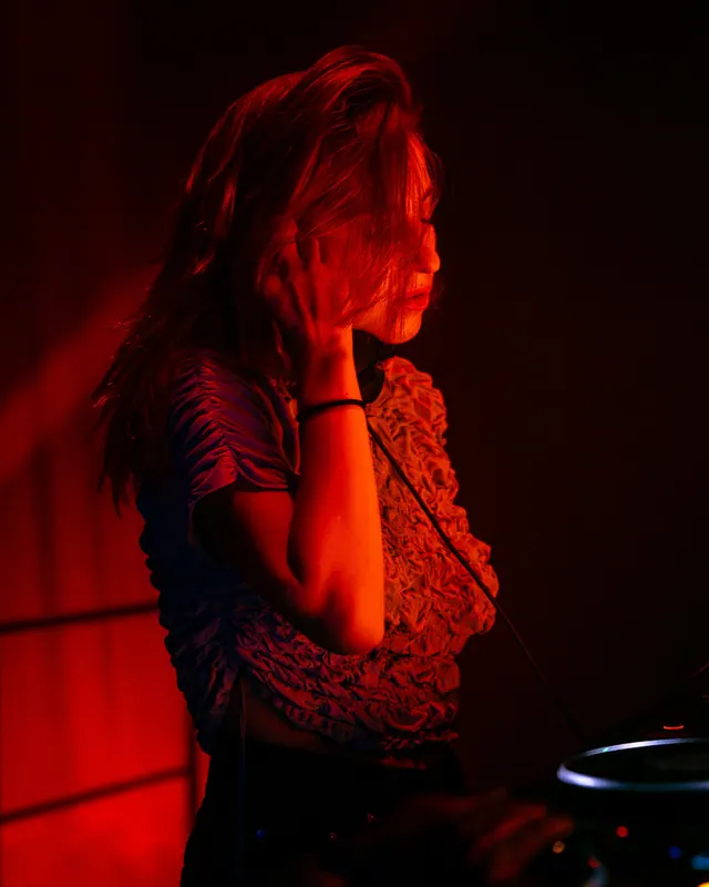 Close detail of a dancer beside a red-lit DJ booth.
