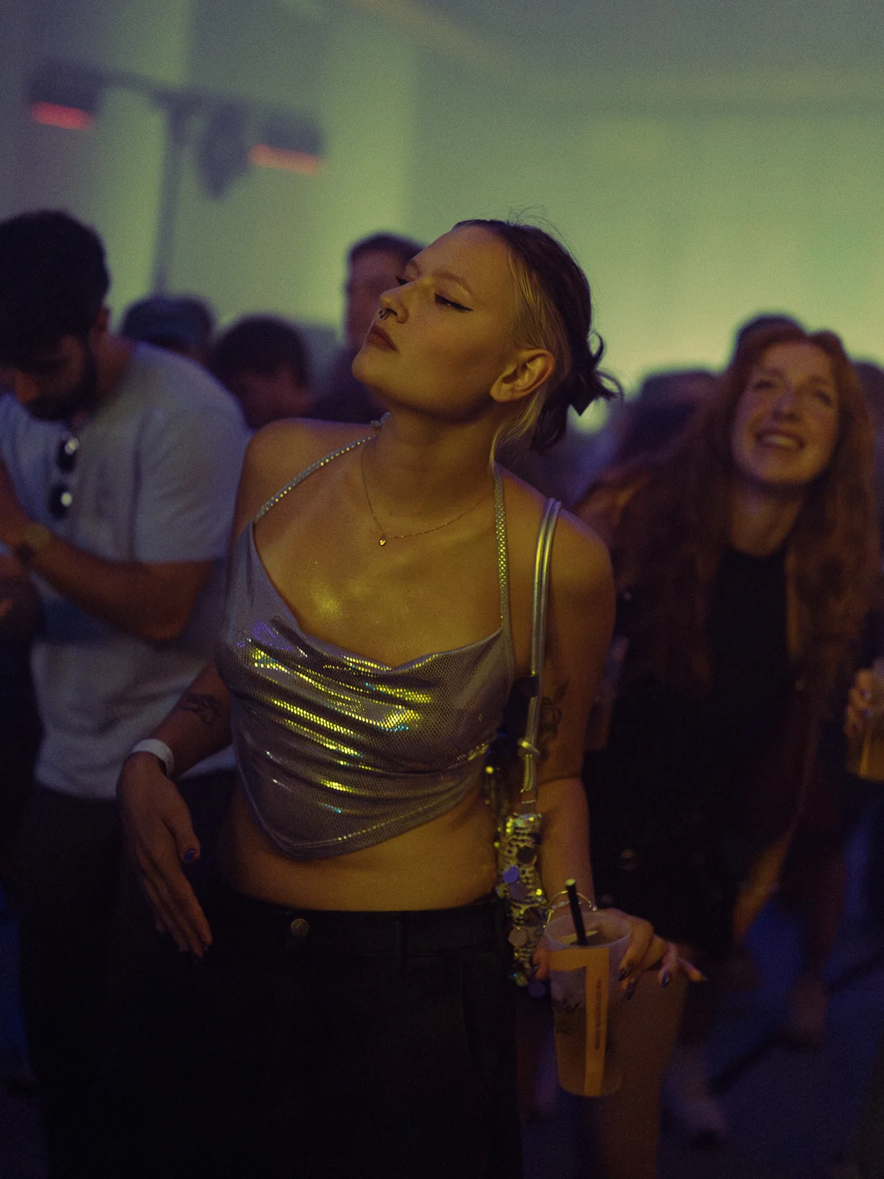 Two friends dancing with eyes closed in soft green and violet light.