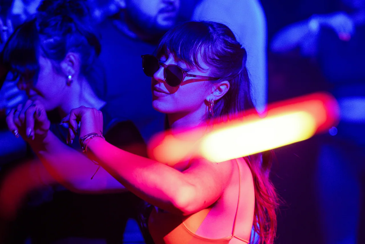 Woman in sunglasses dancing behind a streak of red light.