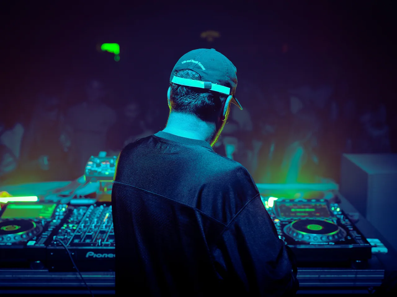 DJ at the decks beneath layered blue and green light.