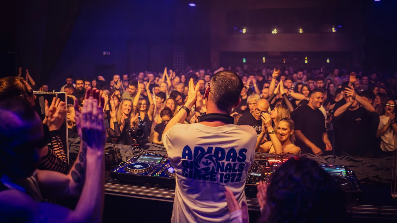 DJ facing a packed audience with hands raised across the room.