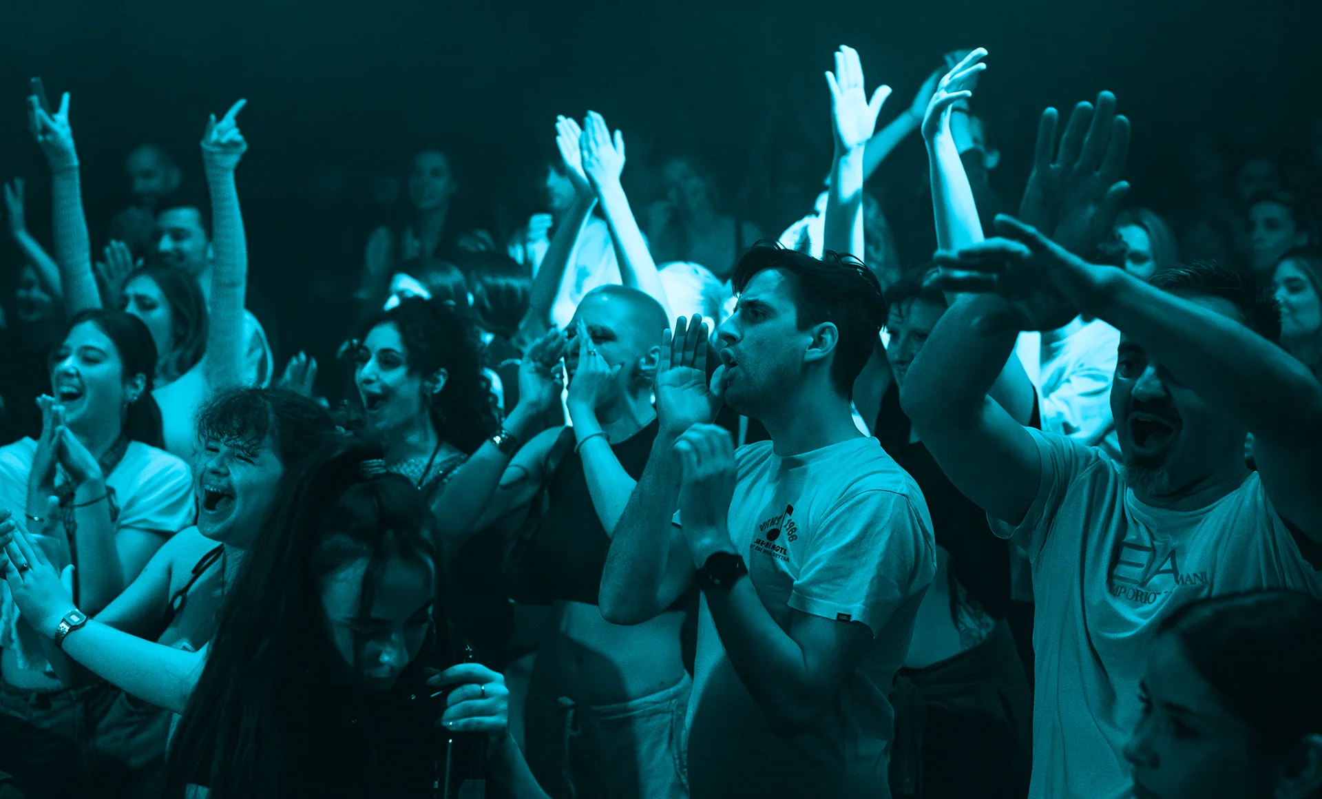 Front-row crowd reaching upward beneath cold blue light.